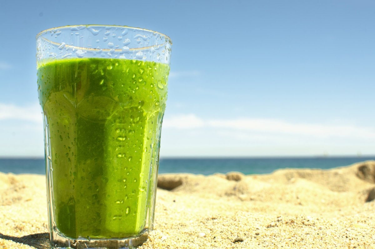 The glass of spinach banana smoothie is on beach | Hurry The Food Up