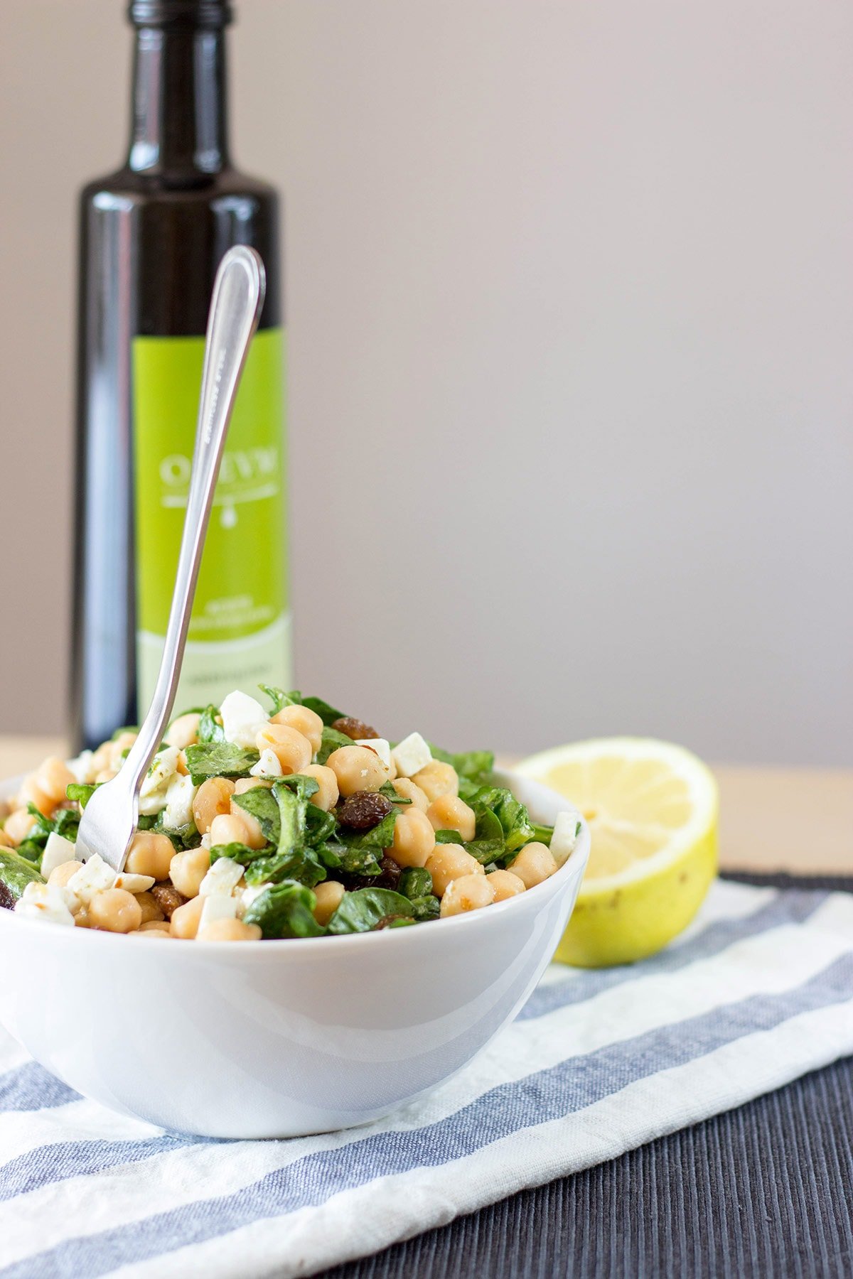 Chickpea Spinach Salad served in a bowl with a bottle of olive oil and a wedge of lemon in the background | Hurry The Food Up