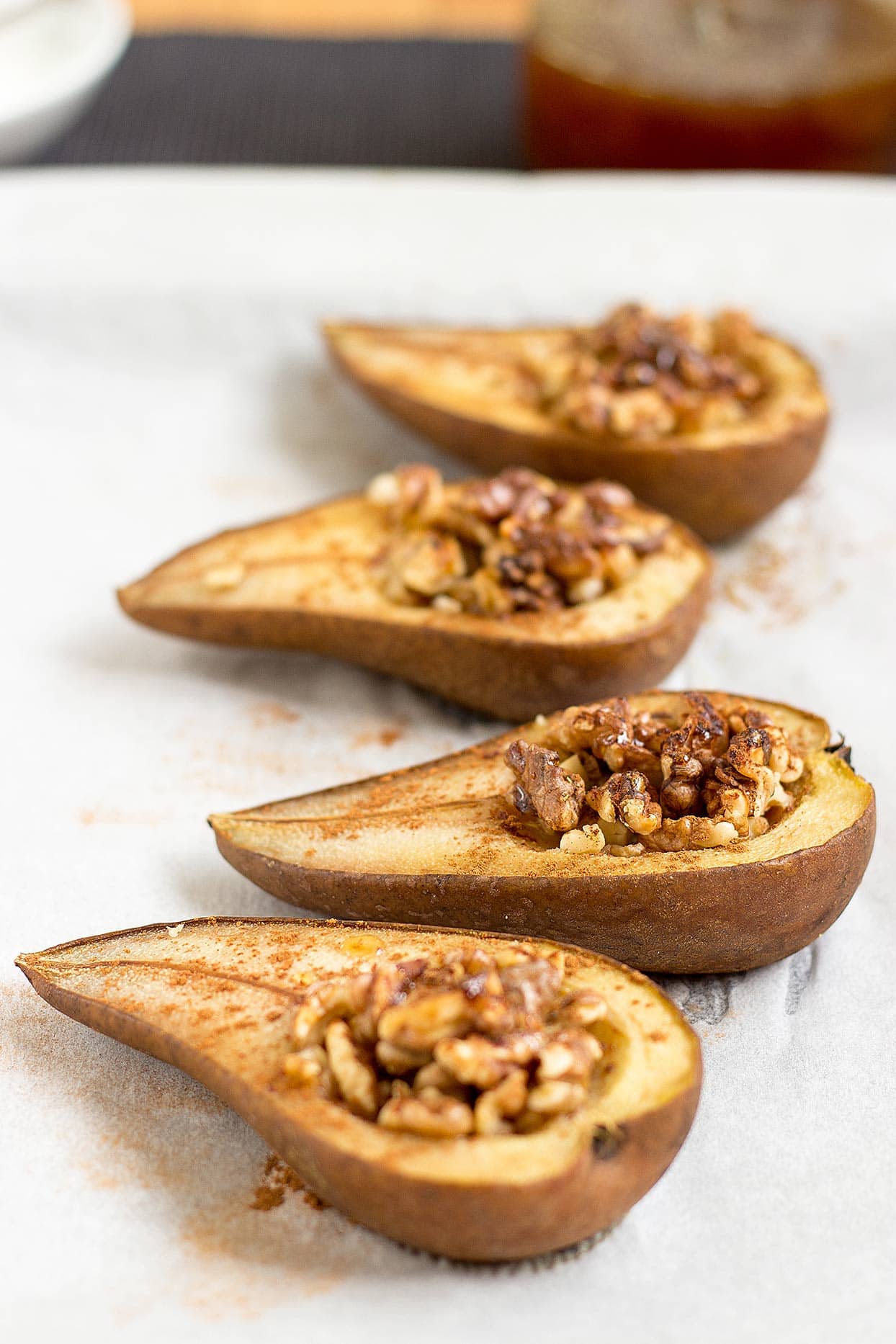 Four pear halves stuffed with walnuts and cinnamon are laid on a white surface | Hurry The Food Up