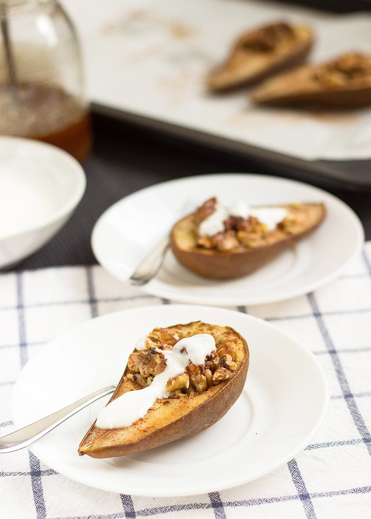 Two pear halves stuffed with walnuts and cinnamon are served on white plates topped with soy yogurt | Hurry The Food Up