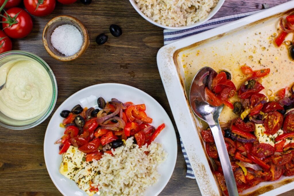 The Bake is served with rice on a table with hummus, tomatoes, olives, baking tray on a towel and a bowl with rice | Hurry The Food Up