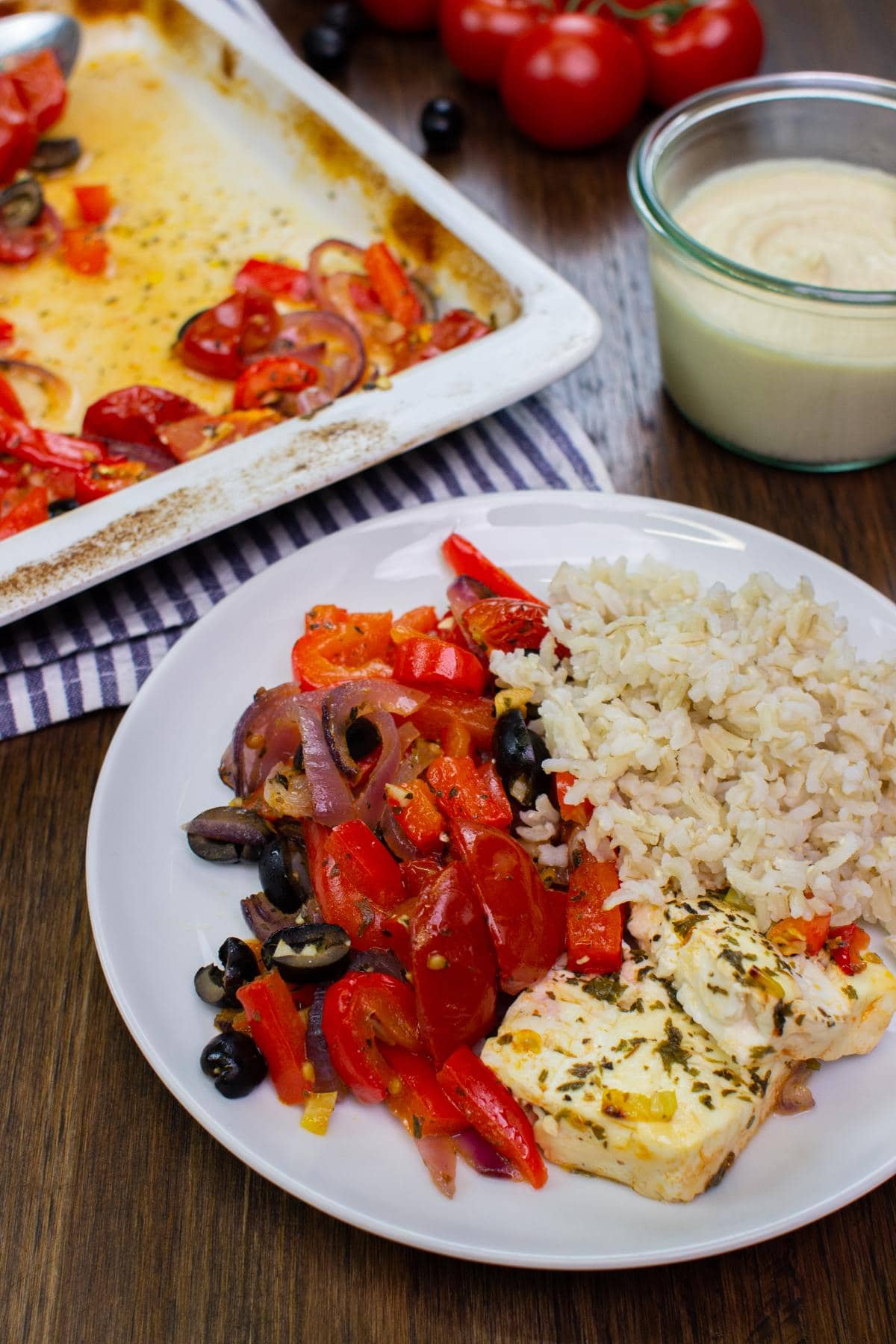 The dish is served with rice on the plate on a table with hummus, tomatoes, olives and baking tray on a towel | Hurry The Food Up