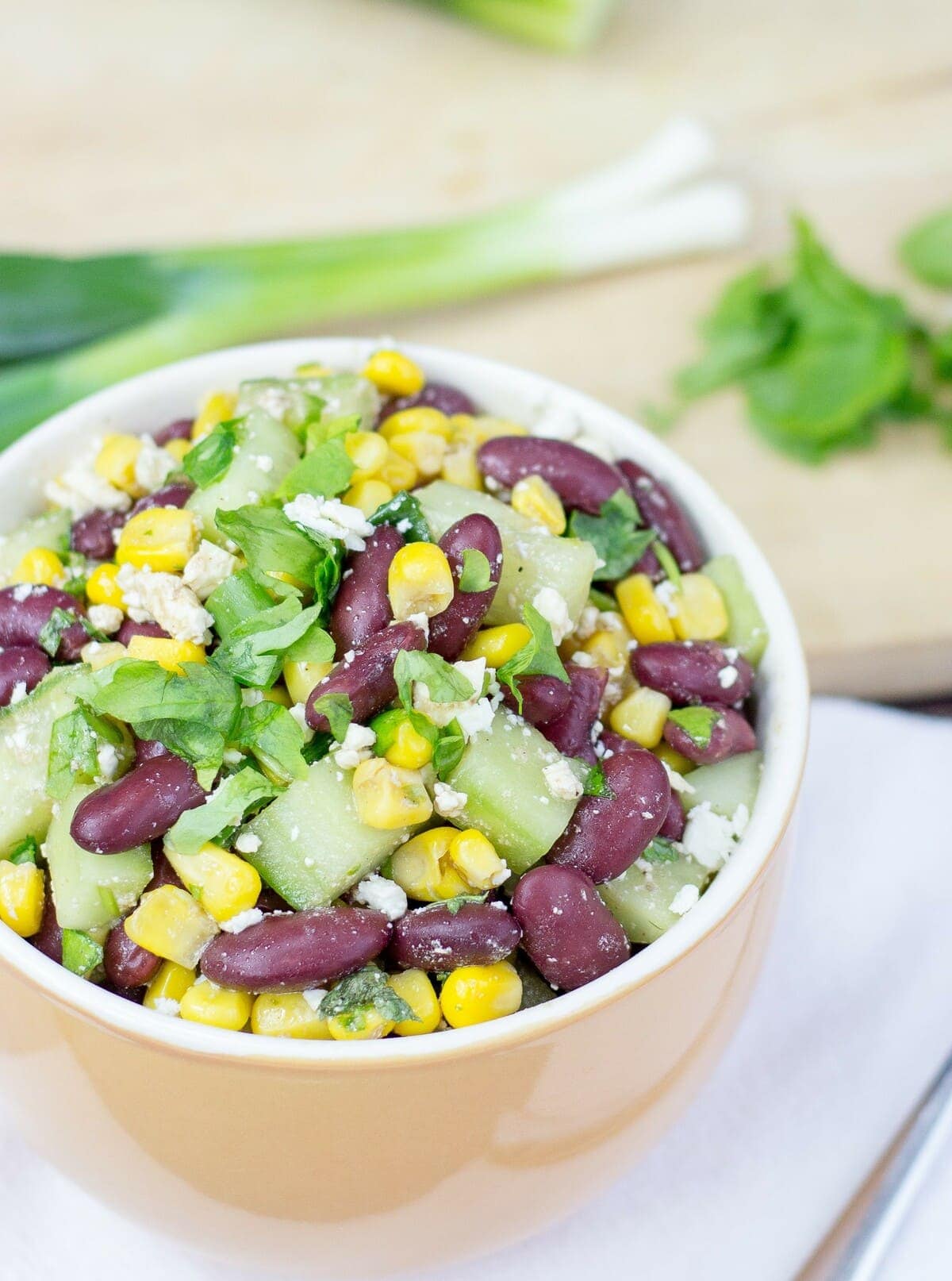 Kidney beans, corn, cucumber dices, parsley and feta cheese are plated in a bowl with spring onions in the distance | Hurry The Food Up 