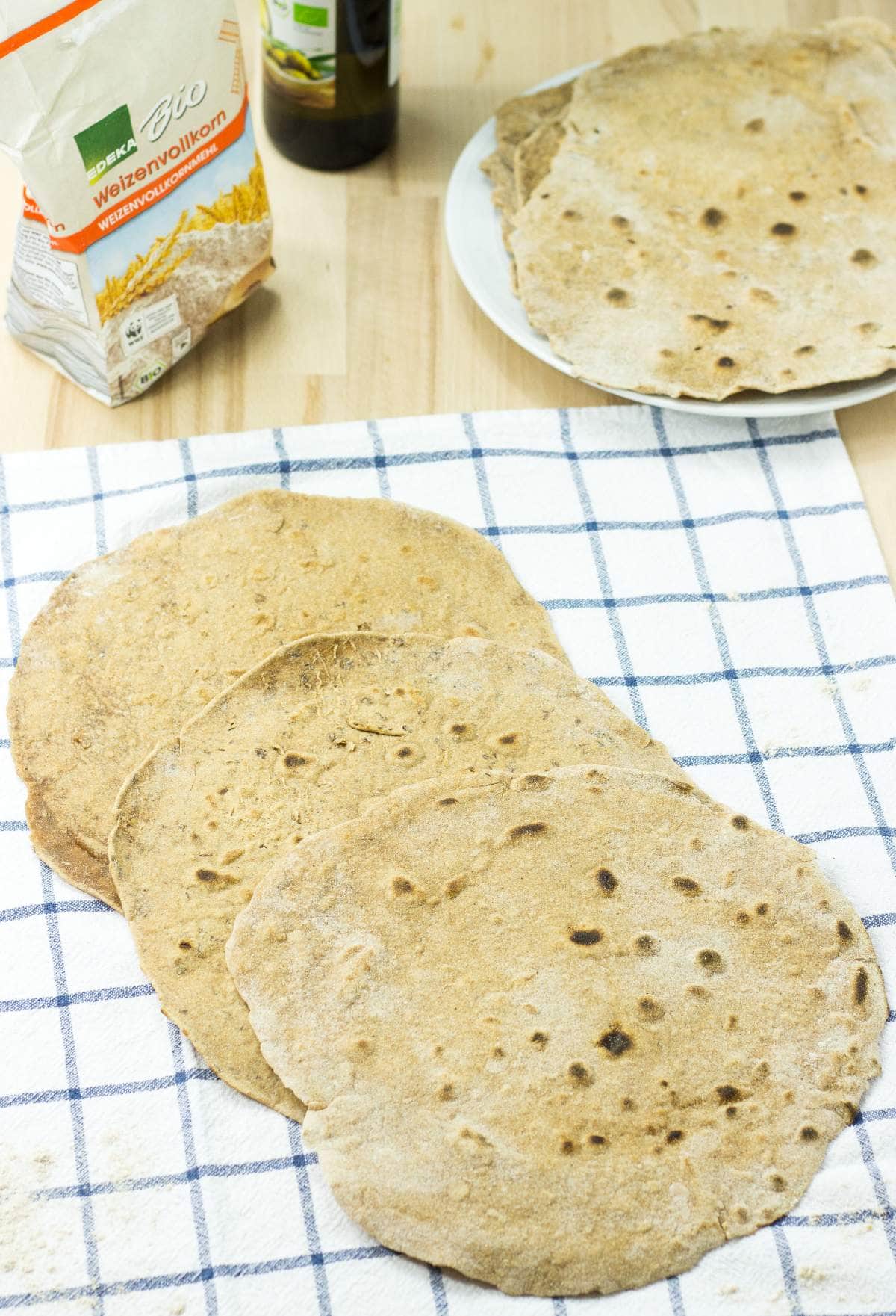 Flour Tortillas lie on the checkered tablecloth. Next to it there are a package of flour, olive oil and a plate with tortillas | Hurry The Food Up