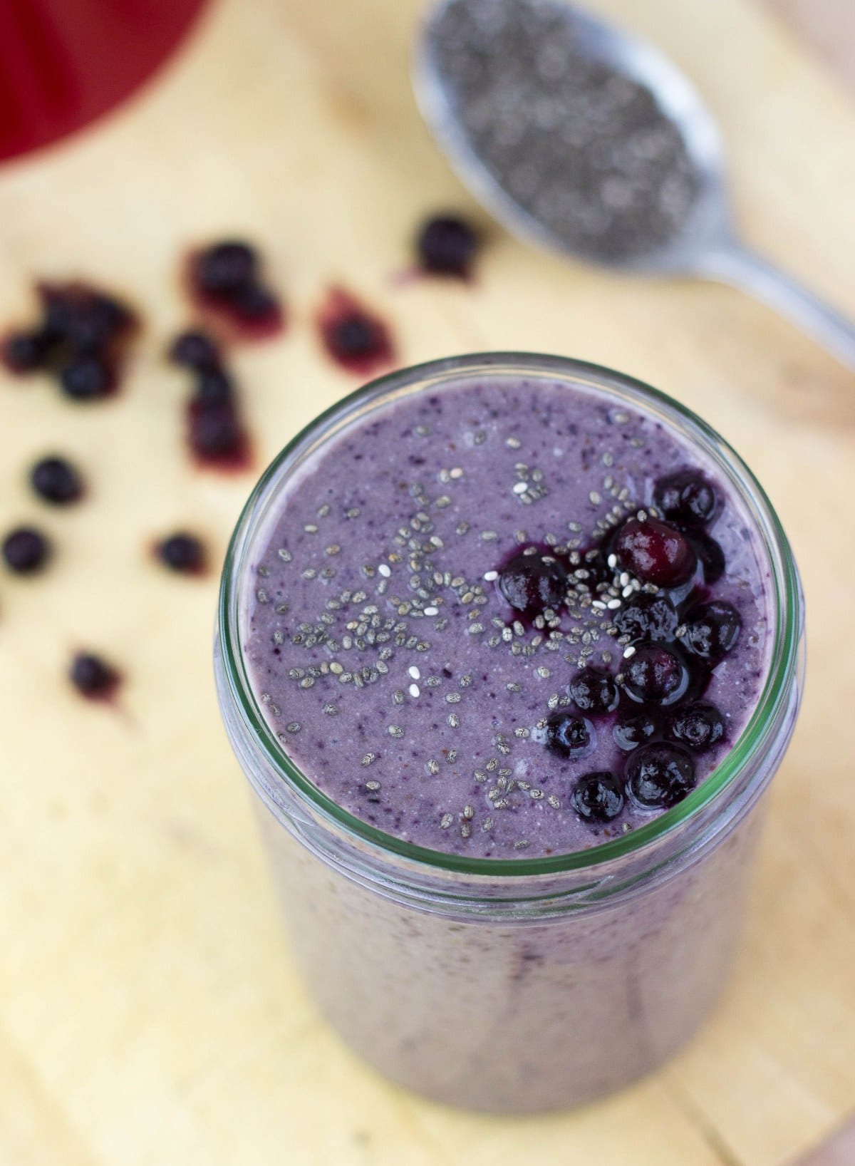 A jar and a small spoon of blueberry banana protein smoothie are on a wooden surface | HurryTheFoodUp