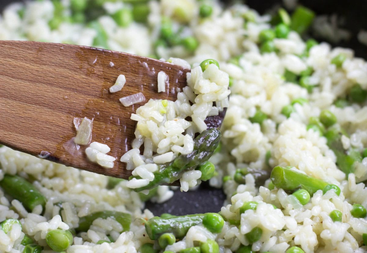 A wooden spoon lifts partly cooked risotto from a pan | Hurry The Food Up