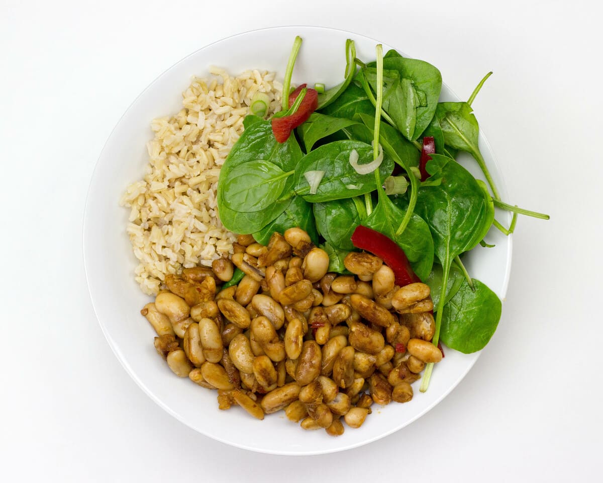 Basmati rice, vegetables and sautéed beans are plated on a white bowl and placed on a table | Hurry The Food Up