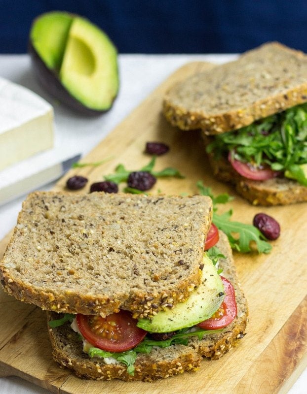 Deux Sandwichs à l'avocat sont prêts sur la planche à découper avec des canneberges et de la roquette | Dépêchez la nourriture