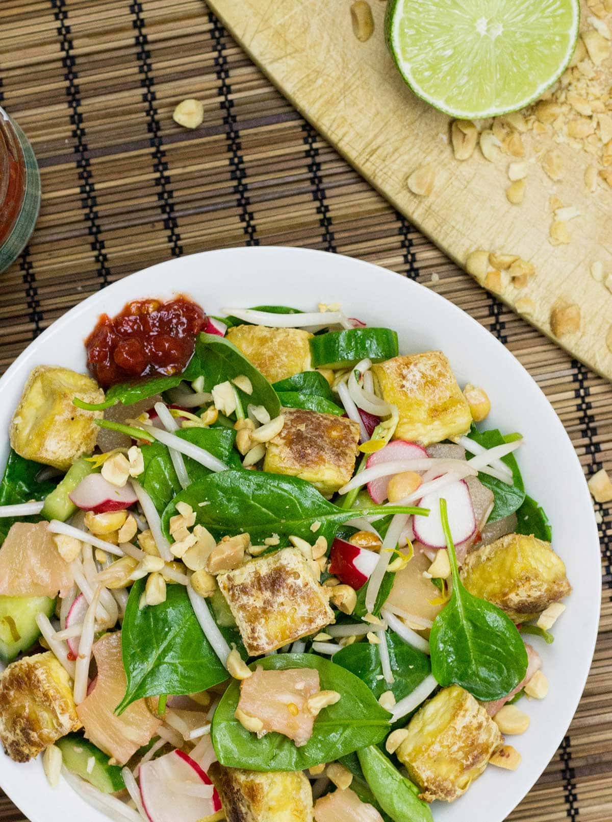 A bowl of Asian tofu salad bird's-eye view next to a slice of lime and some crushed peanuts placed on a cutting board in the top right corner | Hurry The Food Up