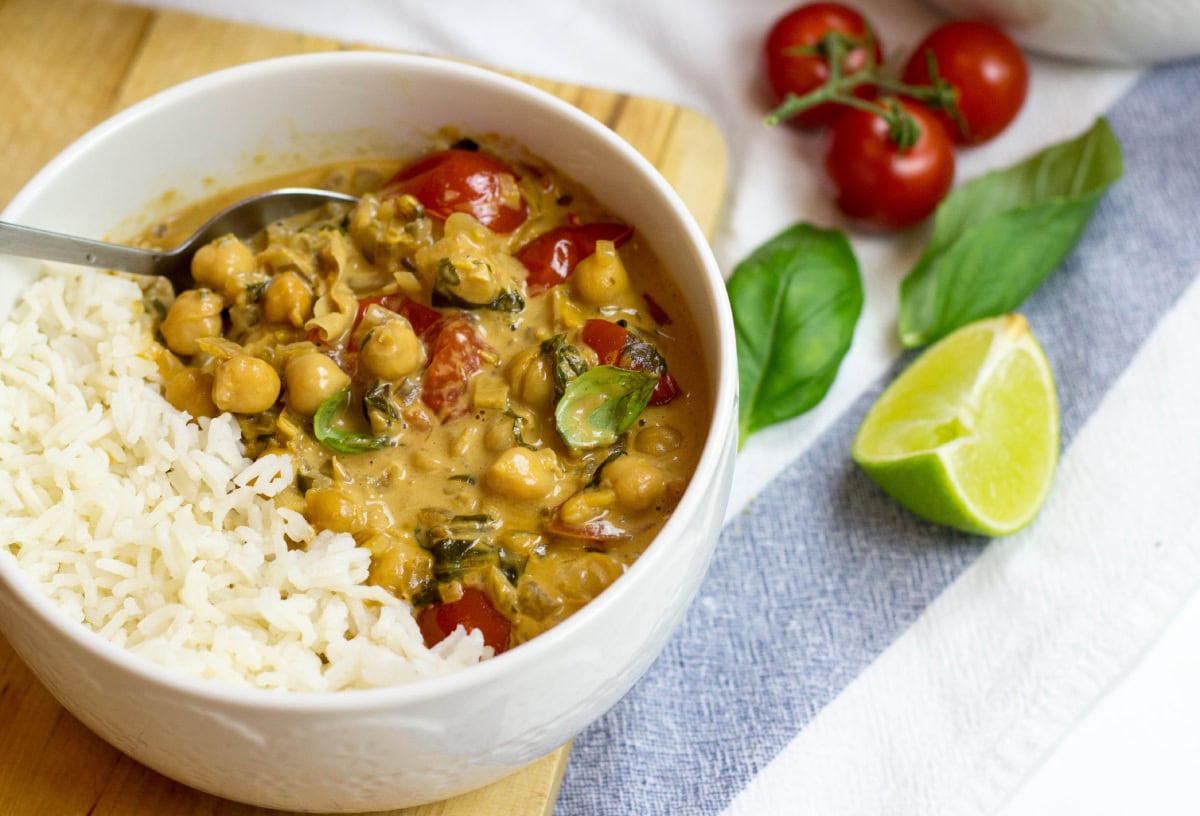 A bowl with Vegan Chickpea Curry. Next to it, there are some tomatoes, fresh basilic leaves, and a piece of lime | HurryTheFoodUp