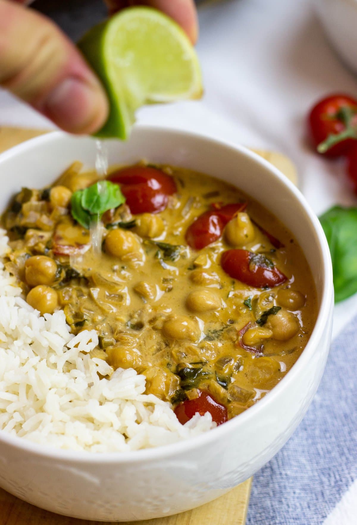 A bowl with Vegan Chickpea Curry. Someone drips lime juice for Curry | HurryTheFoodUp