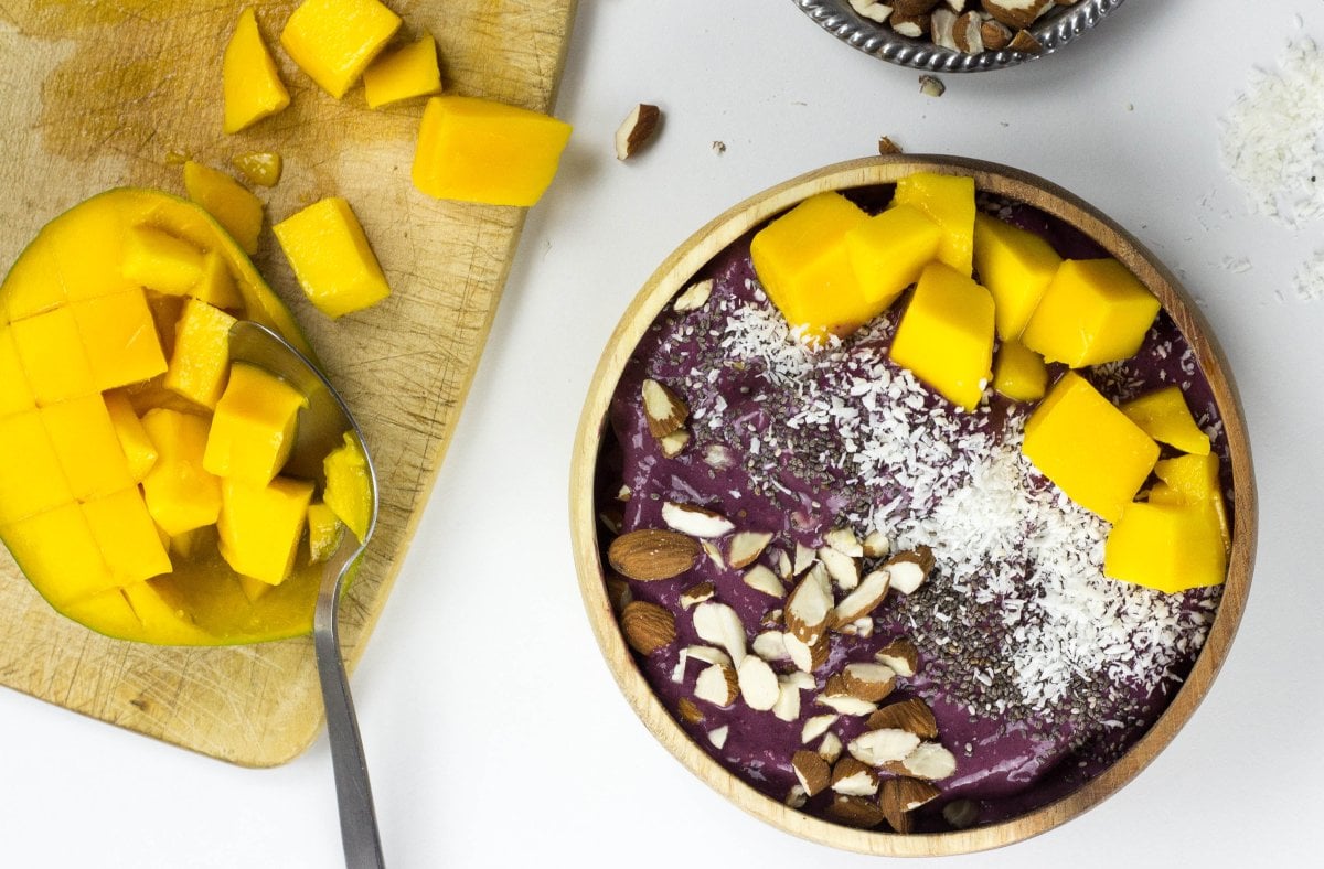 An acai bowl next to a wooden board with chopped mango | Hurry The Food Up