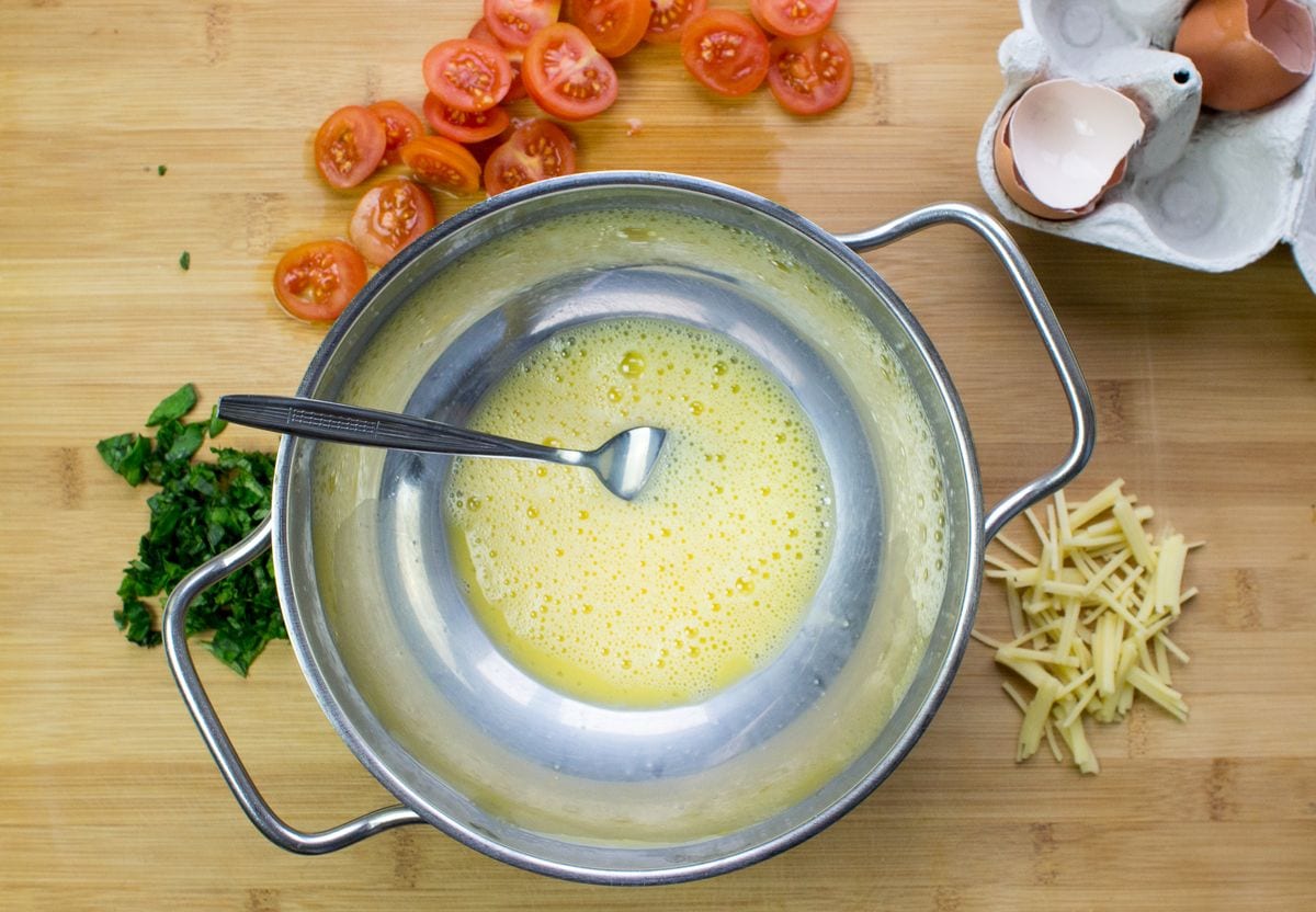 A bowl of whisked eggs on a chopping board with tomatoes and eggs and chopped basil | Hurry The Food Up