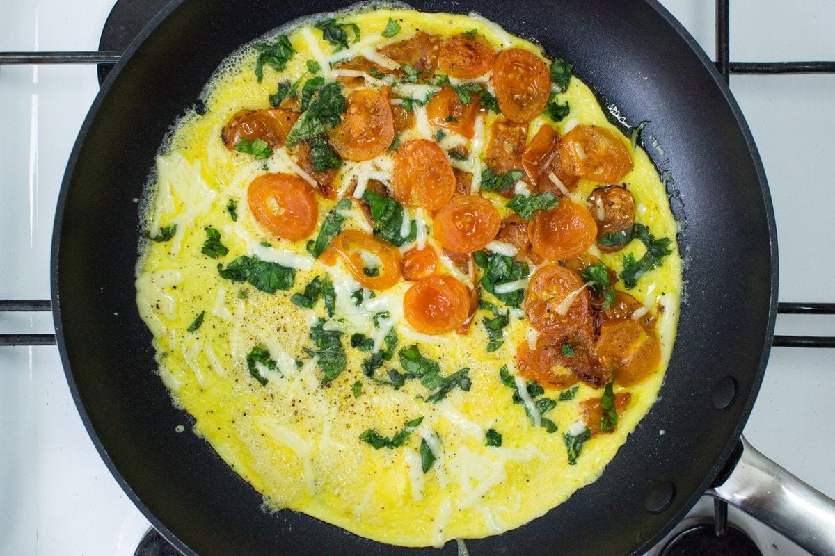 An omelette in a frying pan filled with chopped tomato, basil and cheese. | Hurry The Food Up