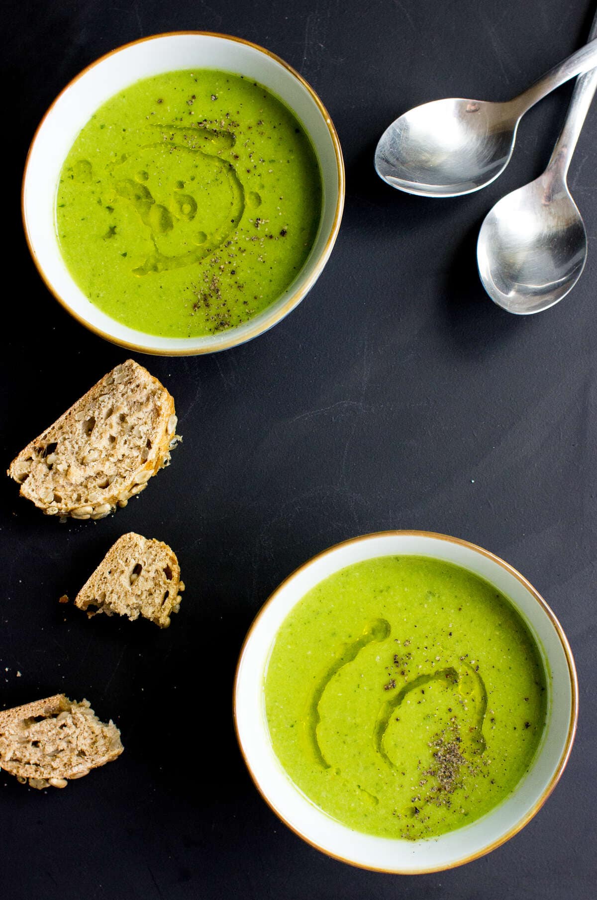 Aerial shot of two bowls of green pea and mint soup, on a black background seasoned with salt and pepper and a drizzle of oil | Hurry The Food Up