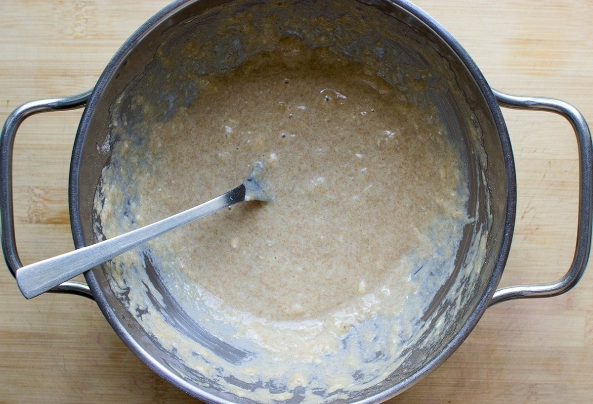 There is a metal pan of banana mug cake batter sitting on a wooden table with a metal fork in the pan | Hurry The Food Up