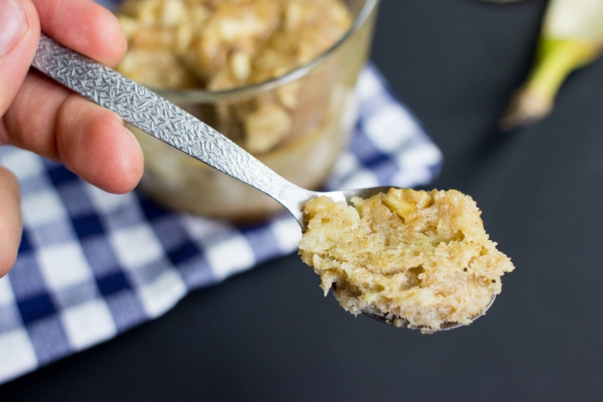 A person holds a spoonful of mug cake up to the camera with the mug in the background on a blue checked cloth | Hurry The Food Up