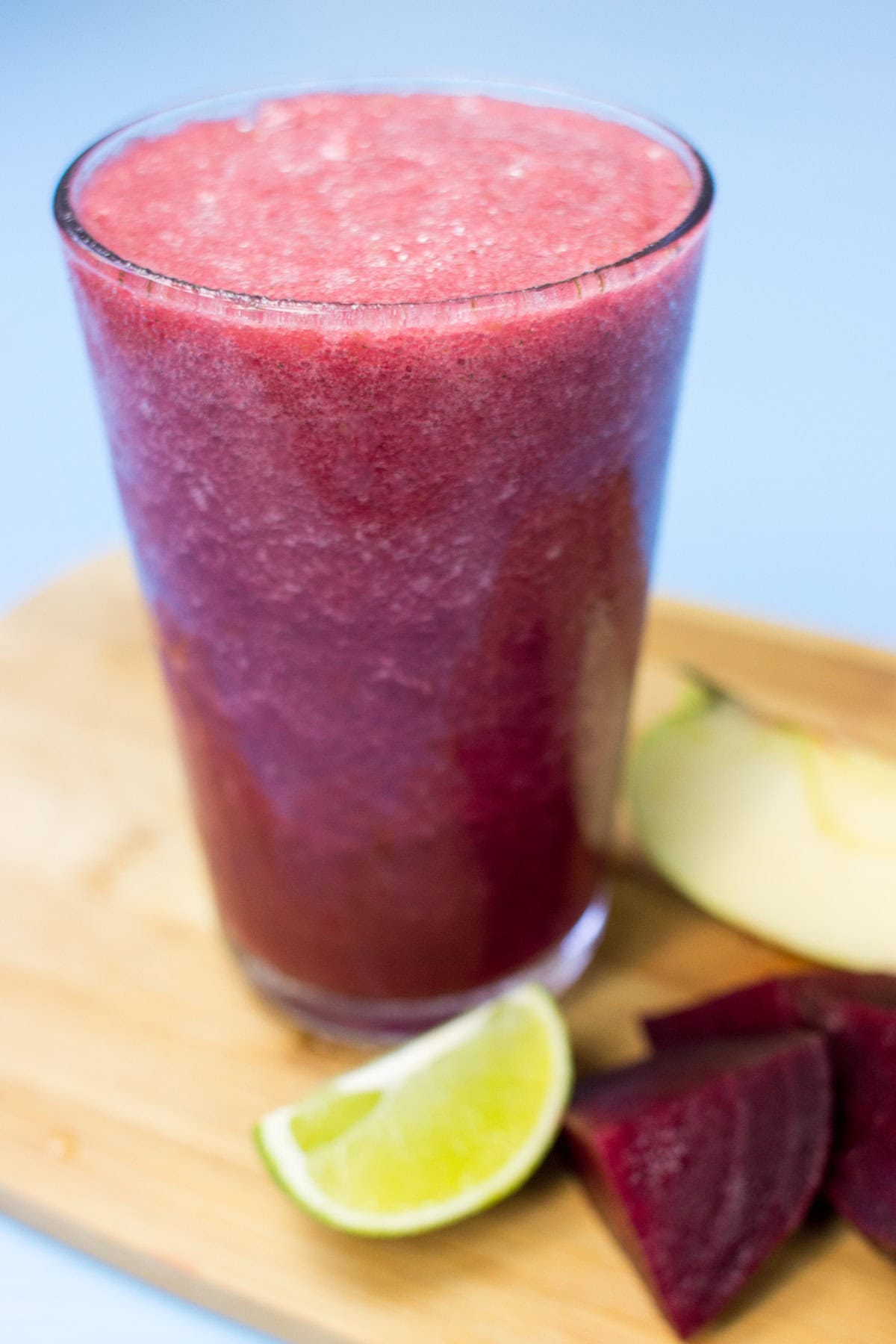 The glass with beetroot smoothie is on the wooden cutting board. There are some pieces of beetroot, lime and apple next to it | Hurry The Food Up