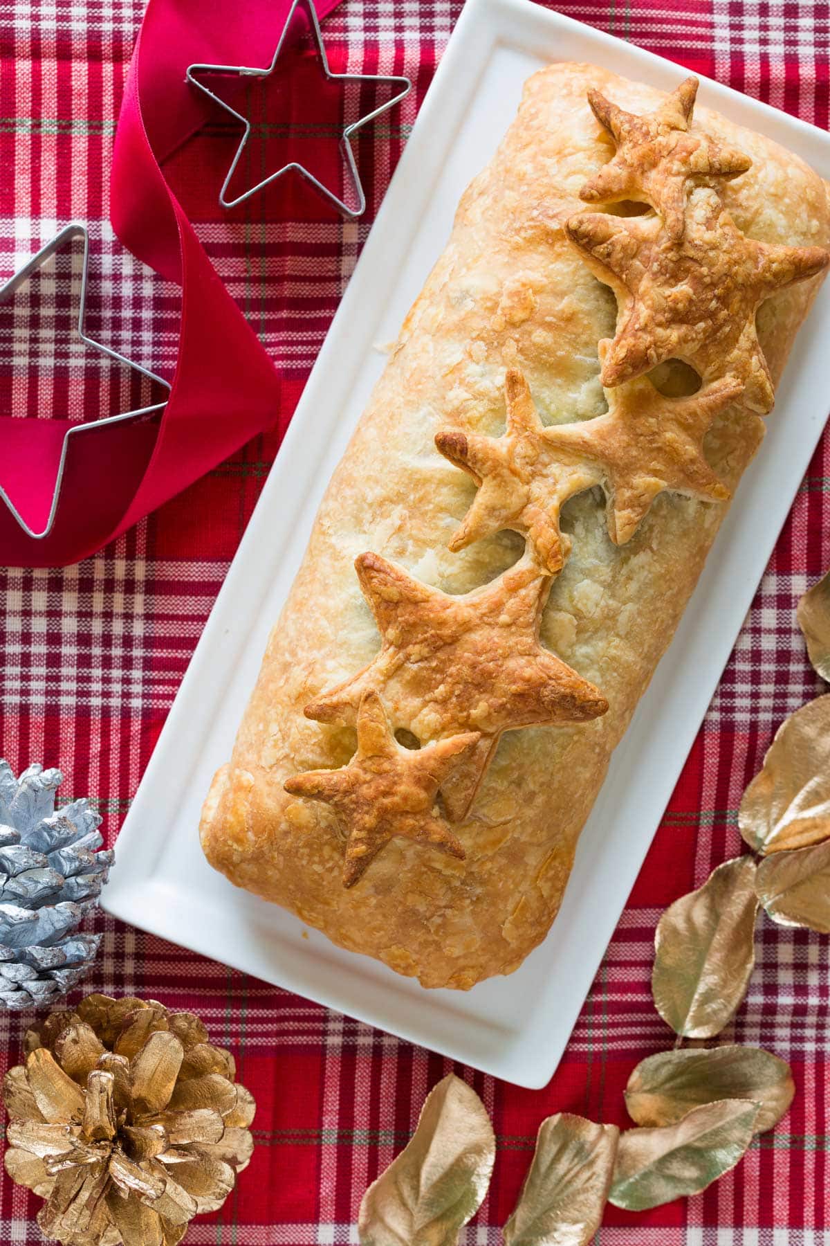 Vegetable Wellington is served on a white plate, which is on the red tablecloth. Around it there are some Christmas decorations | Hurry The Food Up