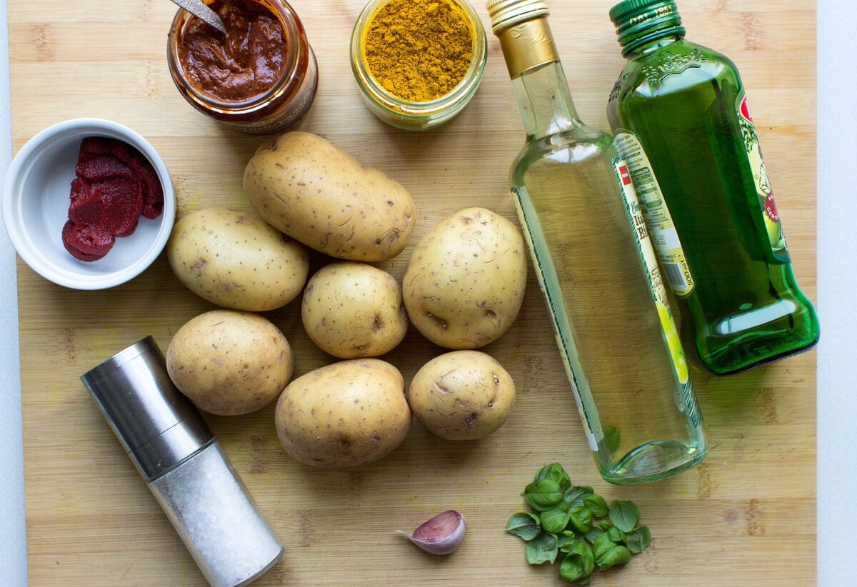 Ingredients for curried potatoes laid out on a chopping board, including potatoes, garlic, salt and olive oil | Hurry The Food Up