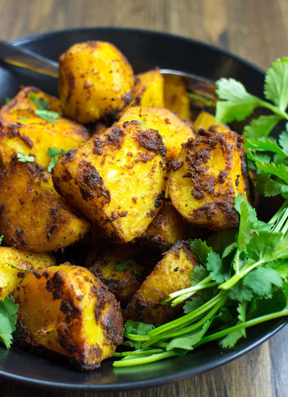 Irish Bombay Potatoes presented in a black bowl with garnish | Hurry The Food Up