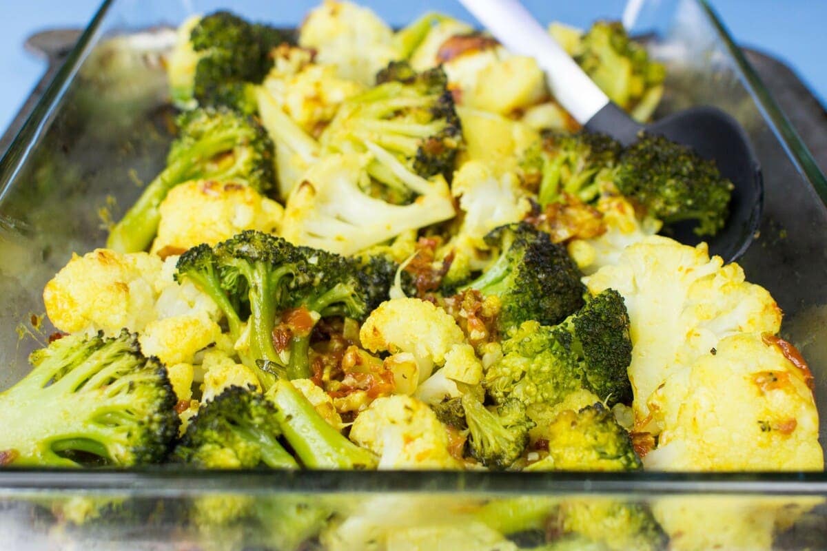 Oven roasted broccoli and cauliflower florets are placed in a glass baking tray over a metal sheet with a spoon in the distance | Hurry The Food Up