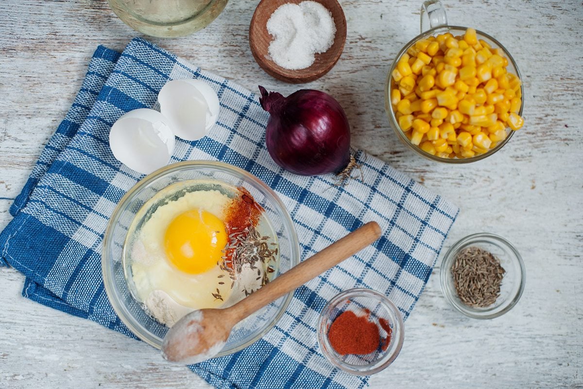 Ingredients to make sweetcorn fritters sit in bowls on a blue checked cloth on a whitewash wooden table | Hurry The Food Up