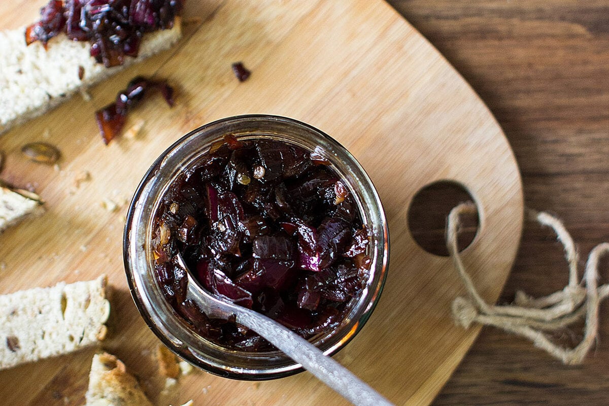 Red Onion Chutney with table spoon are in the jar that is on the chopping board with pieces of bread | Hurry The Food Up