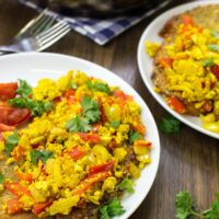 Two plates of scrambled tofu are placed upon a table. A frying pan with tofu scramble is in the distance | Hurry The Food Up
