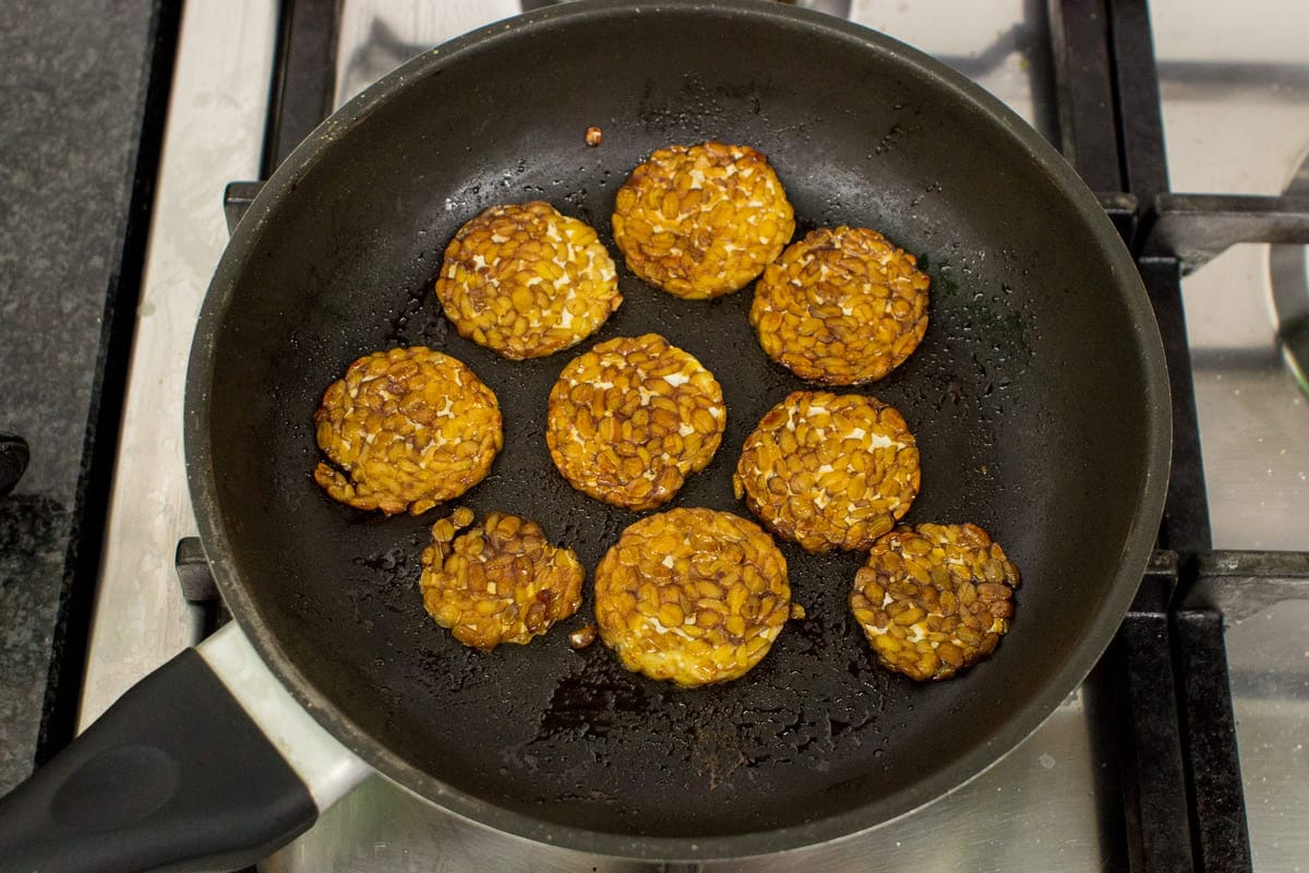 Sliced tempeh are seen frying in a skillet | Hurry The Food Up