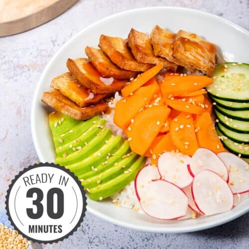 A vegan poke bowl ready to eat, with tofu and veggies layered and drizzled with sweet sesame sauce with time stamp | Hurry The Food Up