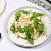 A white plate of couscous and pear salad with goats cheese, with a black fork on a napkin behind it | Hurry The Food Up - 8