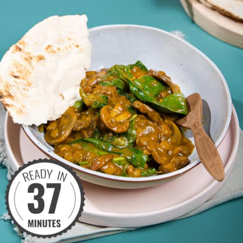 A bowl of stew with a wooden spoon and a piece of torn flatbread on the side with a time stamp in the bottom left hand corner | Hurry The Food Up