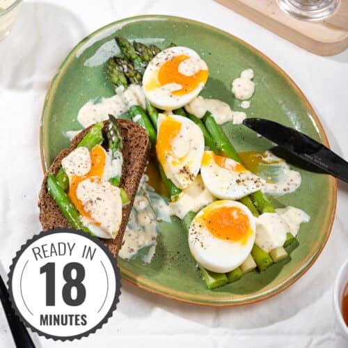 A plate of asparagus, jammy eggs, sour cream sauce and dark bread in the process of being eaten for breakfast with a time stamp in the bottom left hand corner | Hurry The Food Up