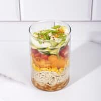 A jar with layers of salad ingredients - seasoning, noodles, corn, carrots, tomatoes, egg, spring onion | Hurry The Food Up