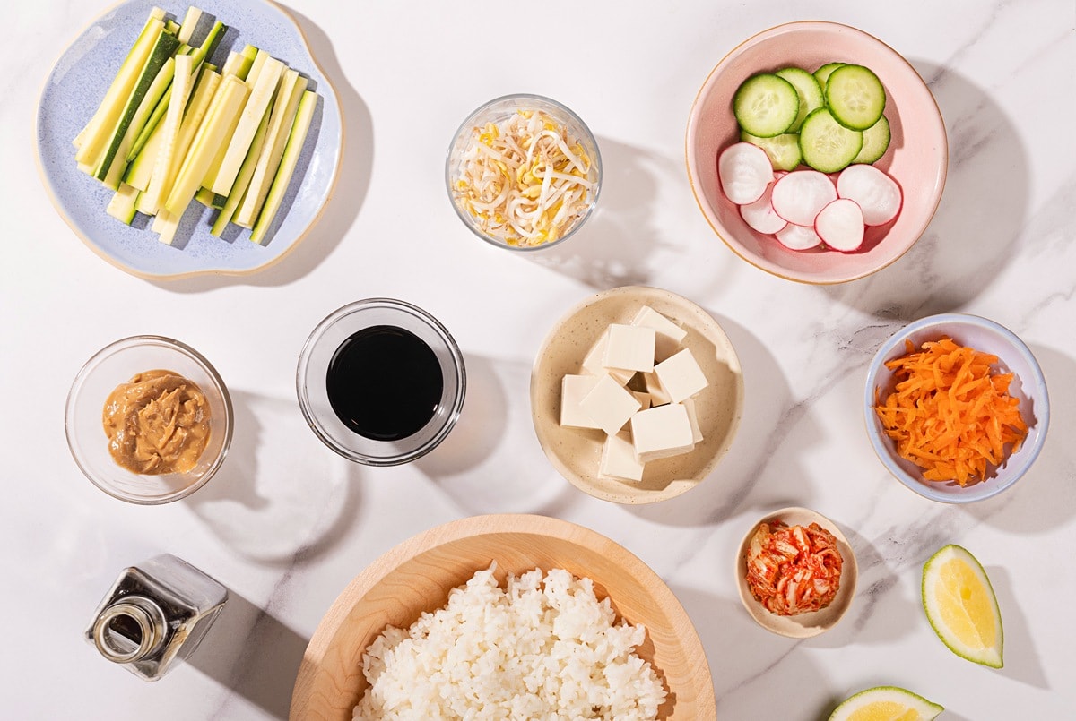 A birds-eye view of all the ingredients for a vegan bibimbap displayed in little dishes on a marbled table | Hurry The Food Up