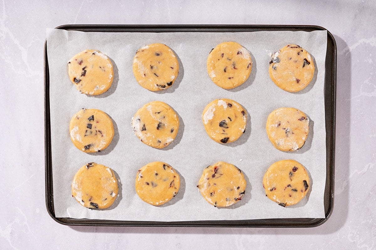 A birds-eye view of a baking tray on a marbled table. On the tray is some cookies on parchment paper, ready to go in the oven to bake | Hurry The Food Up