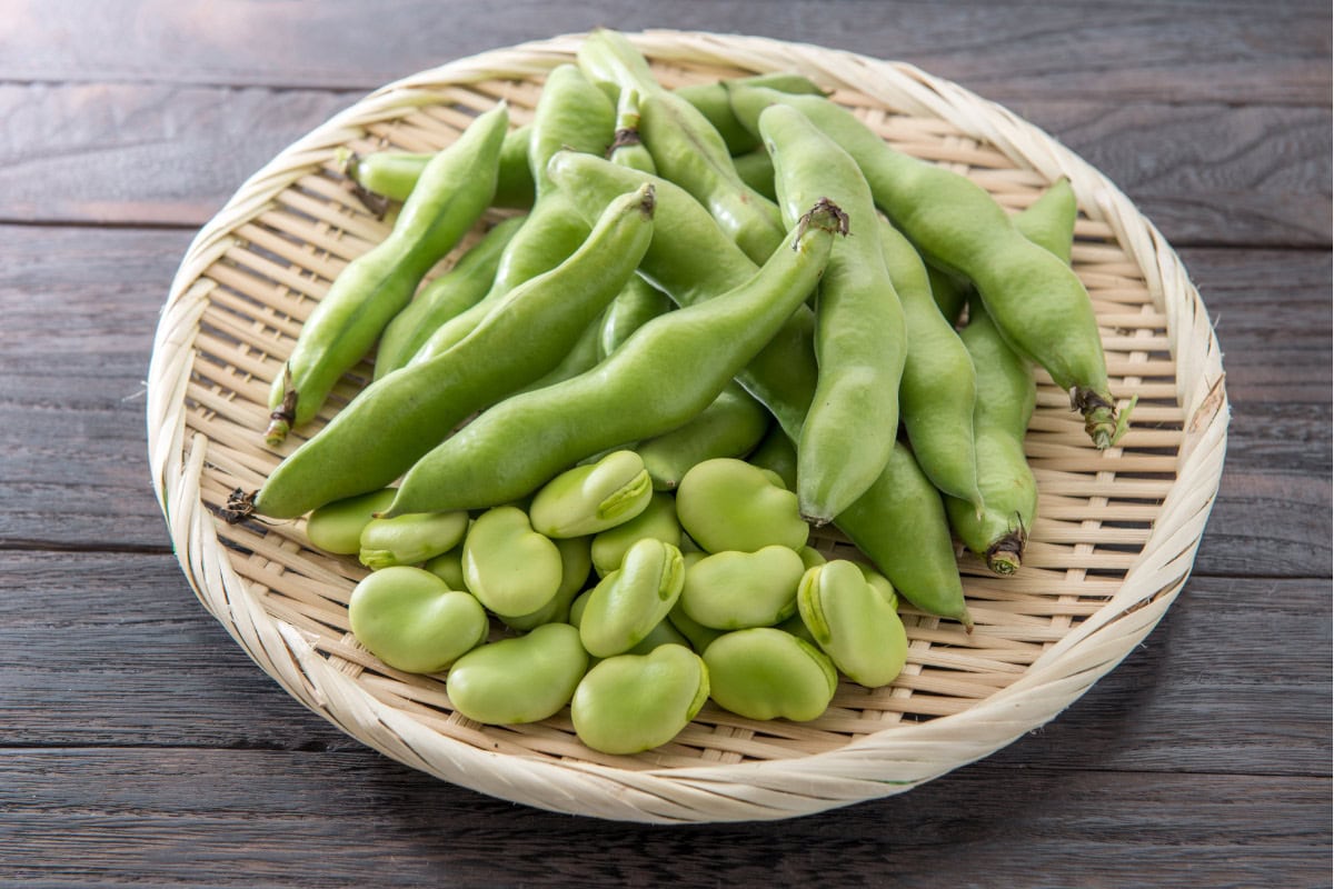 The straw plate with broad beans is on the wooden surface | Hurry The Food Up