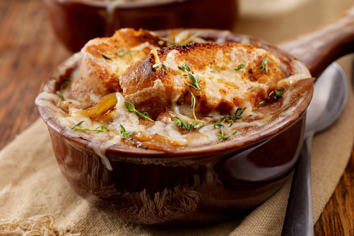 French onion soup is in the porcelain dish. Next to it, there is a spoon | Hurry The Food Up