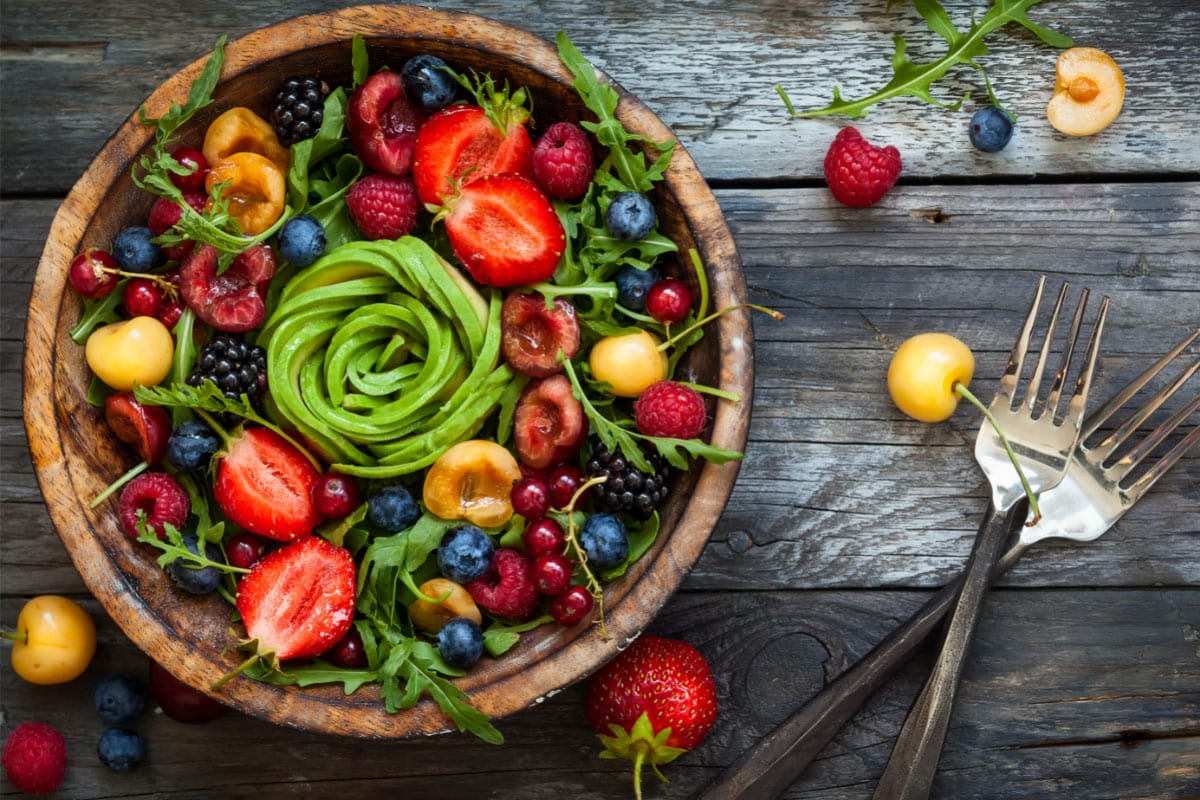 A wooden plate with fruit salad, next to it lie two spoons | Hurry The Food Up