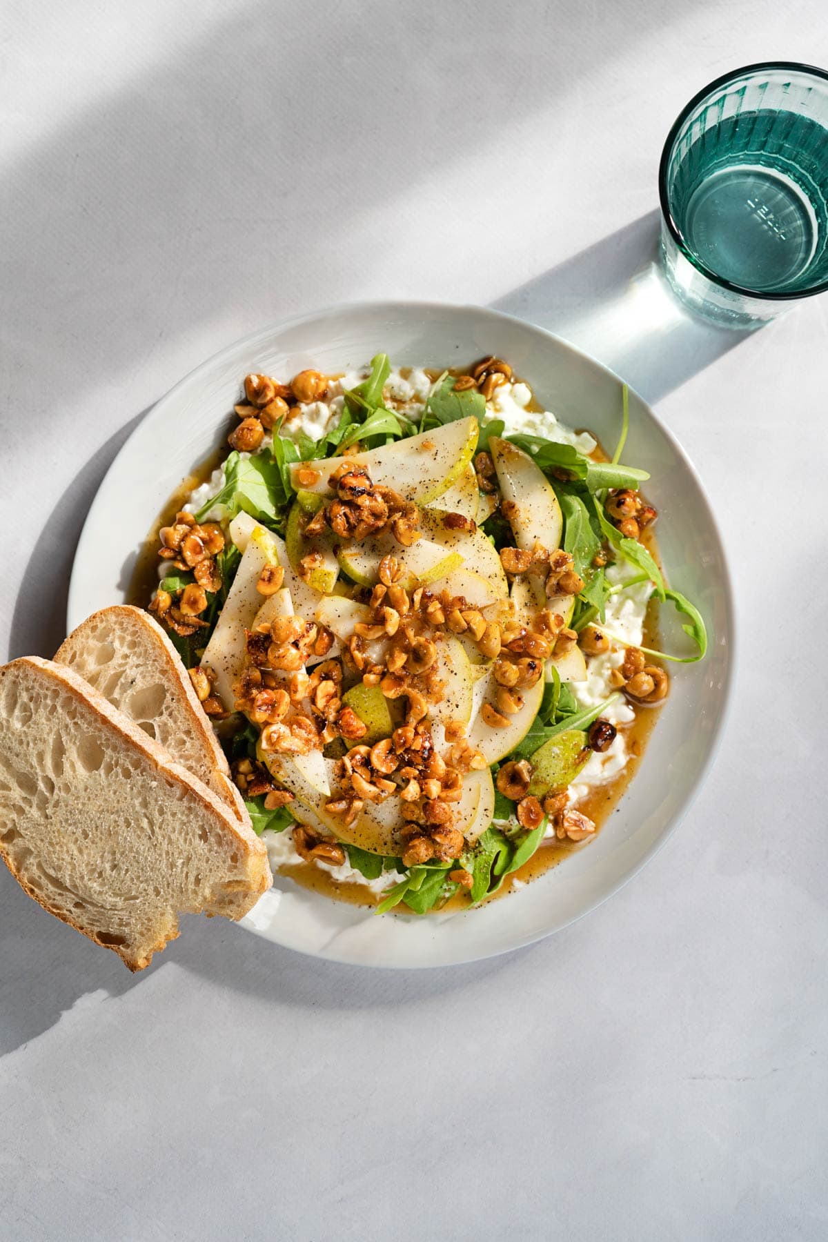 Bird's-eye view of cottage cheese salad and two pieces of bread served on a white plate which is on a light surface. Next to it, there is a glass of water | Hurry The Food Up