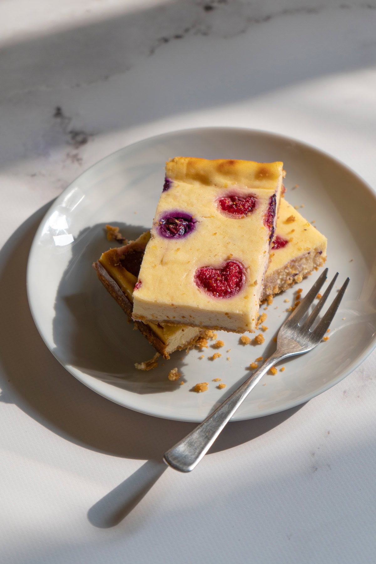 A white plate with two pieces of cottage cheesecake and a fork on the marble surface | Hurry The Food Up