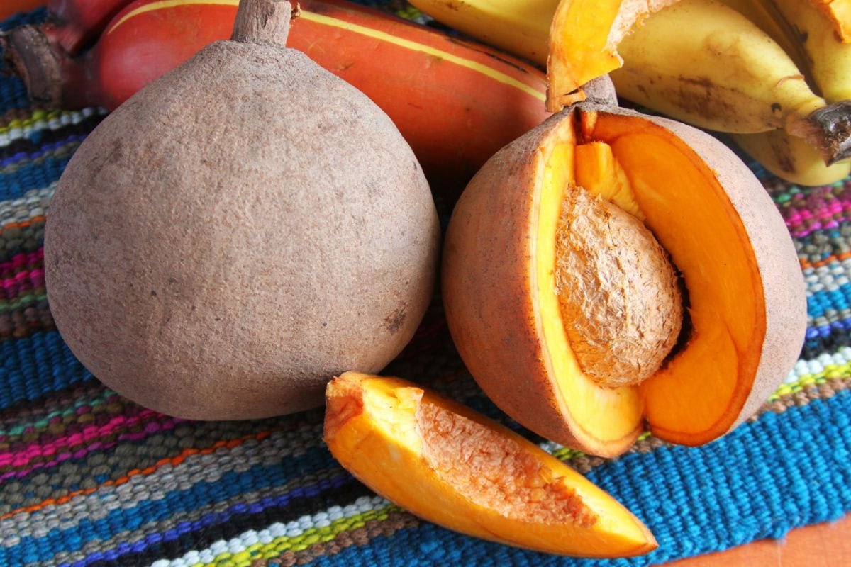 Mamey Sapote fruit with a segment cut out to reveal the stone on a colourful stripy background | Hurry The Food Up