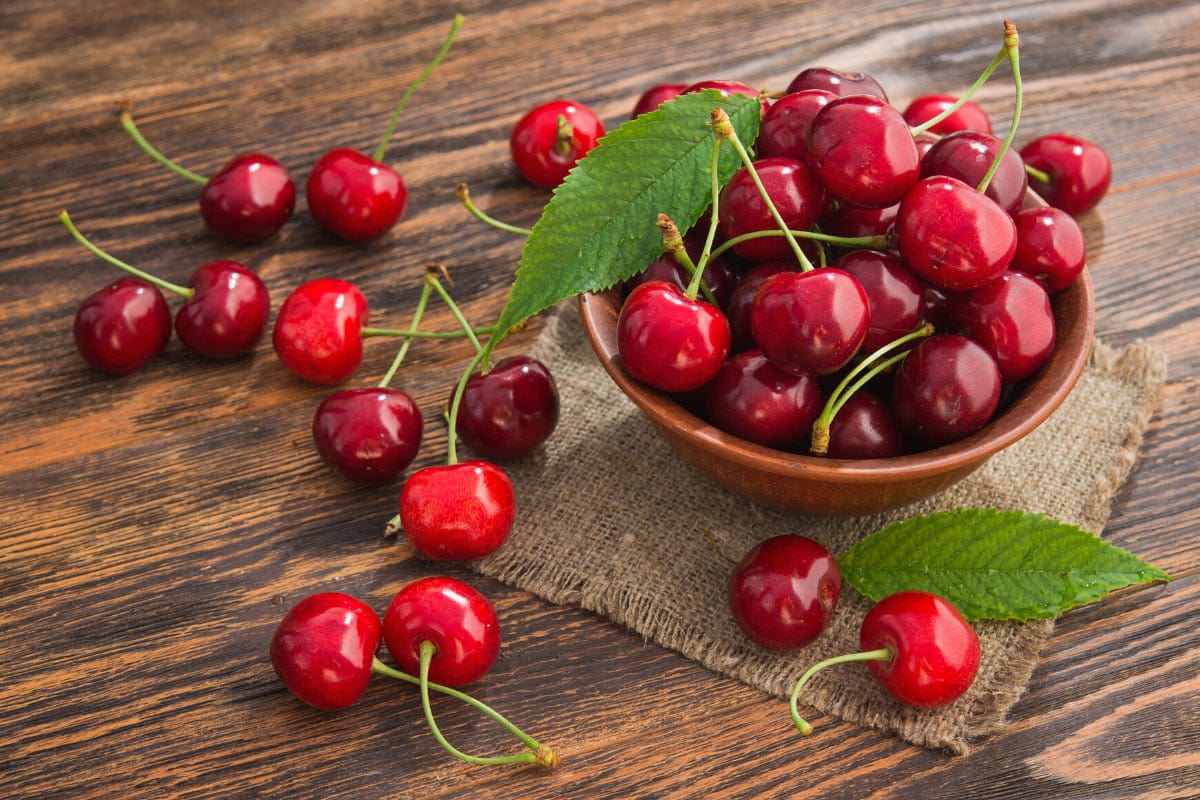 Ripe Afghan cherries lie in the brown bowl, which is on the straw napkin. Around it there are scattered some Afghan cherries | Hurry The Food Up