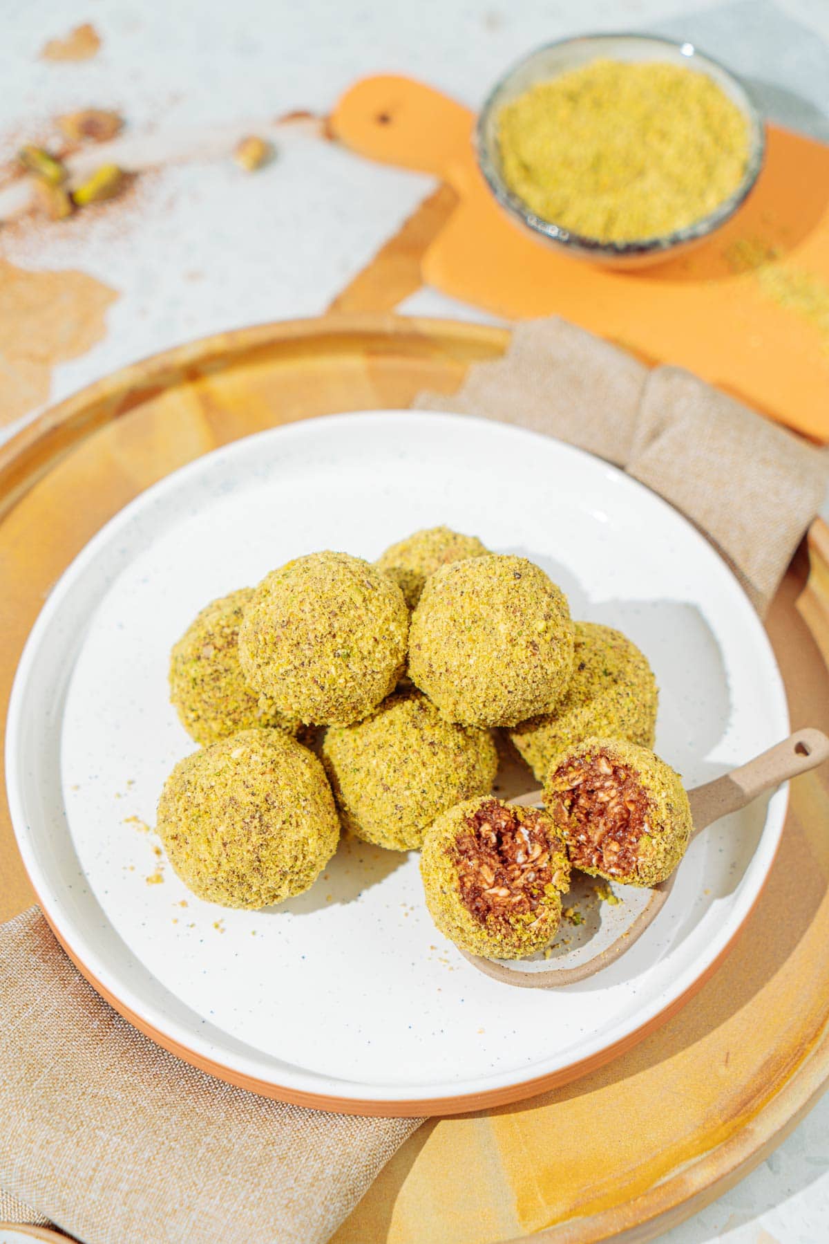 A white plate with peanut butter protein balls that is on the wooden tray with linen napkin under it. Near it there is a small bowl with ground nuts | Hurry The Food Up