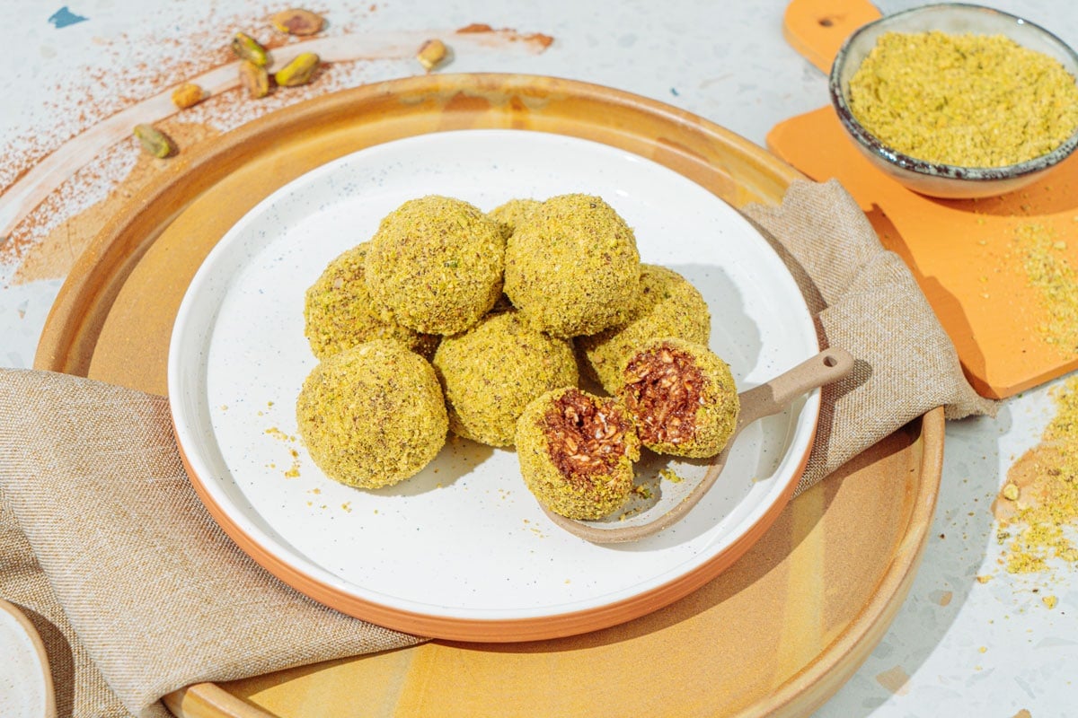 A white plate with peanut butter protein balls that is on the wooden tray with linen napkin under it. Near it there is a small bowl with ground nuts | Hurry The Food Up