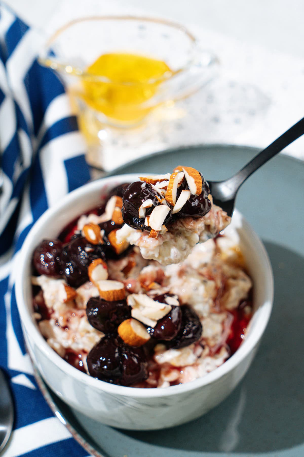 A white bowl with protein oatmeal stands on the plate. Near it, there are colorful napkin and glassware with honey | Hurry The Food Up