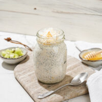 The jar with high-protein overnight oats and the spoon are on the marble сut board. Near it, there are two small bowls with kiwi and honey | Hurry The Food Up - 11