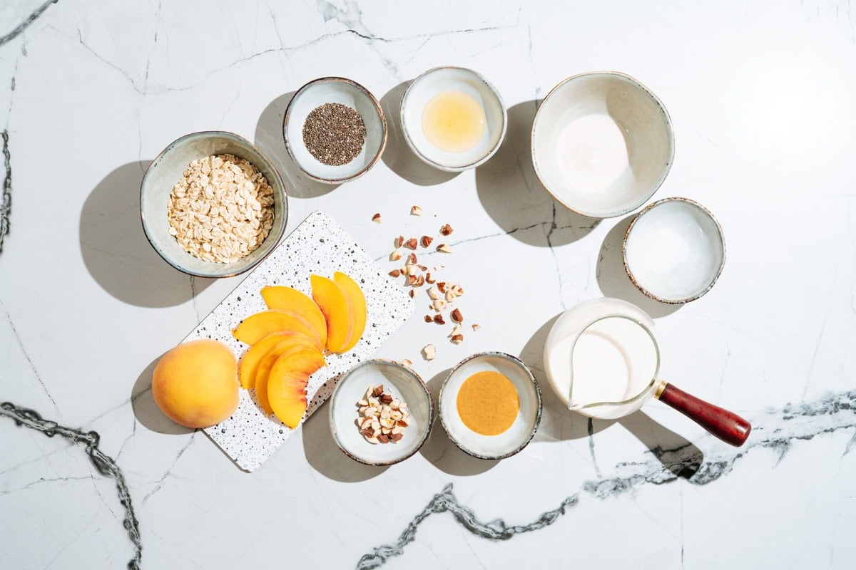 The ingredients for overnight oats with  protein powder like rolled oats, chia seeds, honey, protein powder, soy milk, peanut butter, hazelnuts, peaches etc | Hurry The Food Up