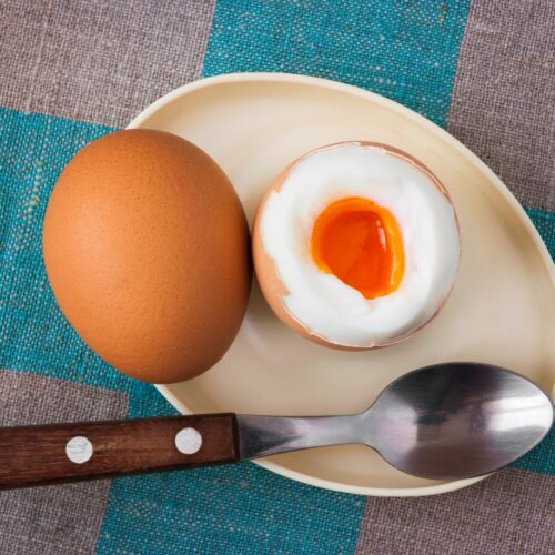 The light oval plate with two boiled eggs and spoon is on the grey-blue surface | Hurry The Food Up